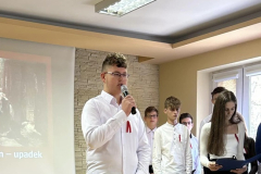 Uczeń stoi na scenie z mikrofonem w ręku, w tle inni uczniowie, napis Rejtan - upadek Polski