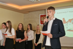 Mężczyzna stoi z mikrofonem w ręku, w tle kobiety