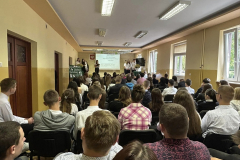 Młodzież siedzi, w tle stoją osoby