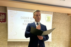 Dyrektor szkoły stoi, w jednej ręce trzyma mikrofon w drugiej teczkę