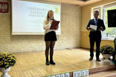 Uczennica stoi z teczka w ręku, obok stoi mężczyzna, w tle ekran rzutnika