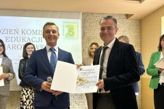 Mężczyźni stoją, w rękach trzymają dyplom, w tle inne osoby