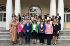 Grupa osób pozuje na stojąco do zdjęcia, w tle filary, okna