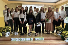 Uczniowie i nauczycielki pozują na stojąco do zdjęcia, w tle żółte kwiaty