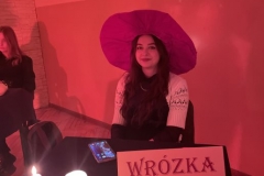 Uczennica w fioletowym kapeluszu siedzi przy stoliku, przed nią napis Wróżka Zuzanna