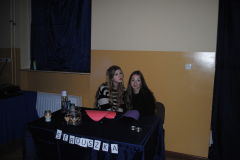 Dwie dziewczyny siedzą przy stole na którym stoją świeczki, słoik