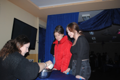 Uczennice stoją, przy stole siedzi dziewczyna, w ręku trzyma świeczkę