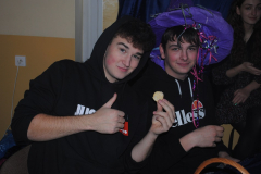 Uczniowie siedzą, jeden trzyma w ręku ciastko, drugi ma na głowie kapelusz