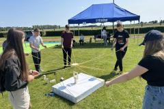 Młodzież stoi, w ręku trzyma sznurki, w tle namiot, żywopłot