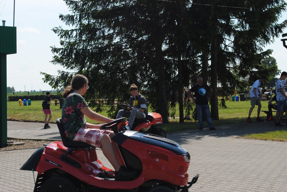 Uczestnicy pikniku jeżdżą ciągniczkami, w tle drzewa