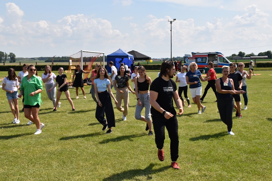 Uczestnicy pikniku tańczą, w tle namioty, karetka