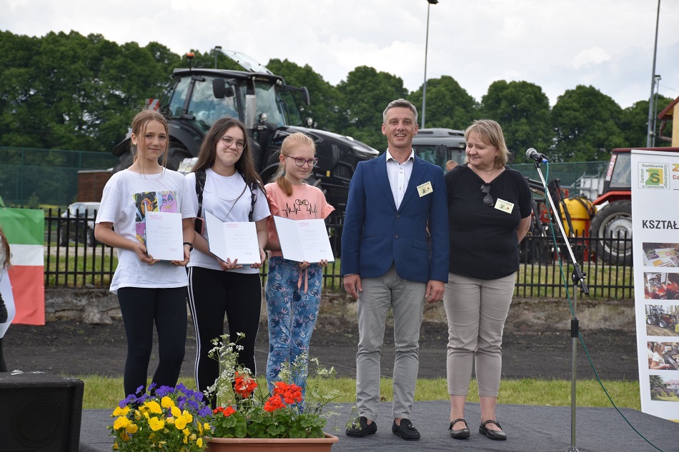 Na scenie stoją: dyrektor ZSCKU w Czarnocinie wraz z nauczycielem oraz uczestnicy pikniku nagrodzeni w konkursie "Powrót do przeszłości", w tle ciągniki, drzewa