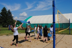 Uczestnicy pikniku trzymają ręczniki i podrzucają balon, w tle hala sportowa