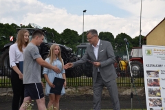 Wicestarosta Powiatu Piotrkowskiego wręcza uczniowi Stypendium Starosty Powiatu Piotrkowskiego, w tle uczennice, ciągniki