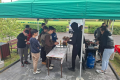 Młodzież stoi przy stole i grillu pod namiotem