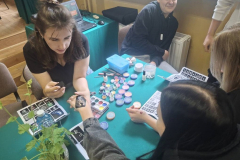 Kobieta trzyma rękę drugiej kobiety, na stole leżą farby