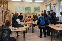 Grupa osób stoi przy ławce na której stoi krowa