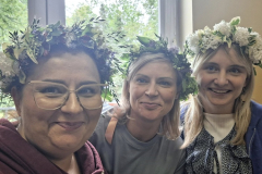 Kobiety w wiankach z polnych kwiatów na głowie, w tle okno