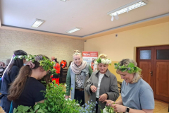 Kobiety w wiankach na głowie stoją przy stole z roślinami