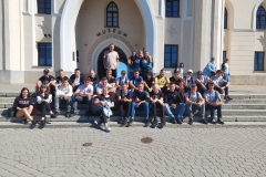Uczniowie siedzą na schodach, w tle ściana, okna