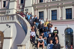 Uczniowie stoją na schodach, w tle ściana, okna