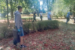 Uczeń z workiem w ręku idzie, w tle inne osoby, drzewa