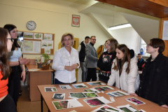 Nauczycielka i młodzież stoją przy ławce na której są porozkładane zdjęcia roślin