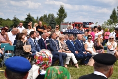Zdjęcie przedstawia osoby siedzące na krzesłach, w tlw drzewa, niebo