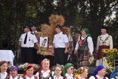 Zdjecie przedstawia strażaków stojących na scenie z wieńcem dożynkowym, obok stoją starości dożynkowi ubrani w ludowe stroje