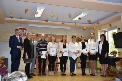Pracownicy szkoły stoją na scenie z dyplomami w rękach