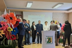 Nauczyciele stoją na scenie obok kwiatów