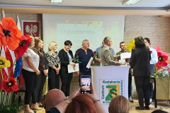 Kobiety i mężczyźni stoją na scenie, w tle kwiaty