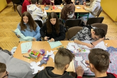 Młodzież siedzi przy stole i zszywa materiał