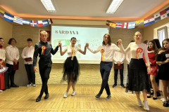 Młodzież tańczy, w tle napis Sardana, obok stoją inne osoby