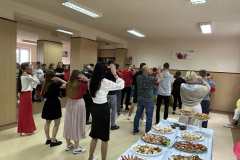 Uczniowie i nauczyciele tańczą, obok na stole stoją potrawy