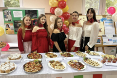 Uczennice w biłao czarno-czerwonych strojach stoją przy stole z potrawami