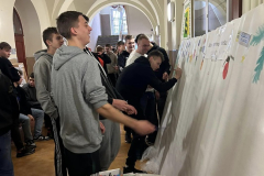 Młodzież stoi przy ścianie z papieru, obok na ławce stoją farby, kredki