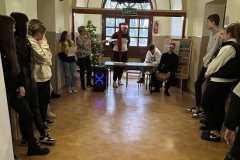 Grupa osób stoi na korytarzu szkolnym, w tle drzwi, choinka