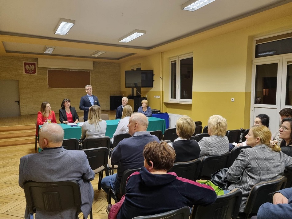 Uczestnicy spotkania siedzą, w tle okna