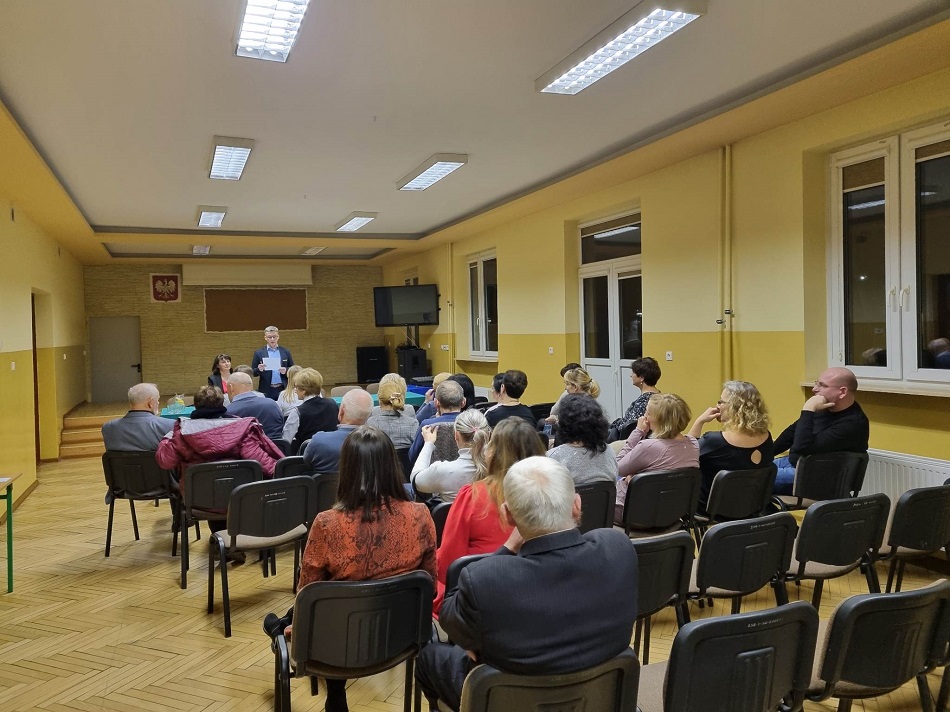 Uczestnicy spotkania siedzą na krzesłach, w tle okna