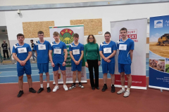 Nauczycielka i uczniowie w niebieskich strojach pozują na stojąco do zdjęcia