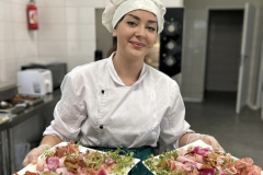 Dziewczyna stoi, w rękach trzyma talerze z potrawami