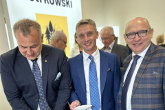 Mężczyzna kroi tort, obok stoi dwóch mężczyzn