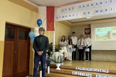 Partner projektu stoi w tle ściana oraz stojący uczniowie