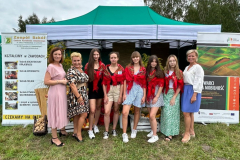 Młodzież i nauczycielki stoją przed namiotem, obok baneru z wymienionymi kierunkami kształcenia w szkole