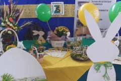 Zdjęcie przedstawia zająca i jajo z drewna oparte o stolik, na stoliku stoi donica z kwiatkiem, rzeżucha w skorupkach jajka