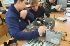 Uczniowie siedzą, na ławce przed nimi leżą komputery