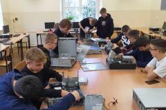 Uczniowie siedzą, na stole przed nimi leżą komputery, w tle okno