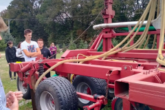 Młodzież stoi przy czerwonej maszynie rolniczej, w tle drzewa