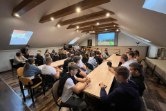 Uczniowie siedzą przy stole, w tle ekran rzutnika